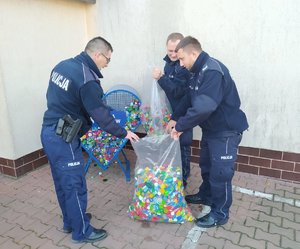 Trzech umundurowanych policjantów opróżnia serce na nakrętki, przesypując je do worków.