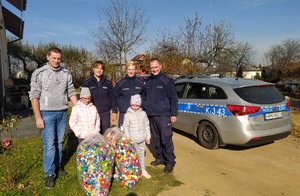 Zdjęcie przedstawia trzech policjantów, mężczyznę i dziewczynkę, której przekazane zostały nakrętki.