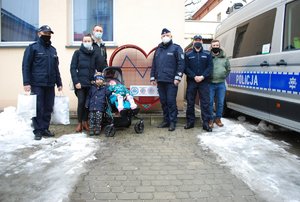 Na zdjeciu od lewej stoją w umundurowaniu służbowym  przedstawiciel Międzynarodowego Stowarzyszenia IPA Region Rzeszów KMP w Rzeszowie, mama i tato Emilki a przed nimi w wózeczku siedzi Emilka, a bok niej stoi braciszek Antoś. Kolejny stoi Komendant Miejski Policji w Rzeszowie insp. Bogusław Kania, obok inicjator akcji, obydwaj w umundurowaniu służbowym, a za nim przedstawiciel Niezależnego Samorządnego Związku Zawodowego Policjantów. Pomiędzy stojącymi na tle ściany budynku stoi pojemnik w kształcie serca na nakrętki. Z prawej strony stojących widoczny jest zaparkowany oznakowany radiowóz - Ambulanse Pogotowia Ruchu Drogowego