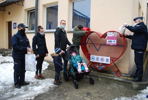 Na zdjeciu przed pojemnikiem w kształcie serca od lewej stoją w umundurowaniu służbowym przedstawiciel Międzynarodowego Stowarzyszenia IPA Region Rzeszów KMP w Rzeszowie, mama i tato Emilki z dziećmi. Za nimi przedstawiciel Niezależnego Samorządnego Związku Zawodowego Policjantów wsypuje do pojemnika nakrętki. Z prawej strony pojemnika nakrętki wsypuje, Komendant Miejski Policji w Rzeszowie insp. Bogusław Kania.