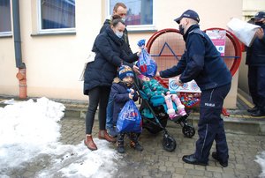 Na zdjeciu na tle pojemnika-serca inicjator akcji policjant z wydziału do walki z przestępczością gospodarcza wręcza upominki dla Emilki i jej braciszka. Za nimi stoją rodzice. Na drugim polanie przedstawiciel Międzynarodowego Stowarzyszenia IPA Region Rzeszów KMP w Rzeszowie wysypuje do pojemnika nakrętki.