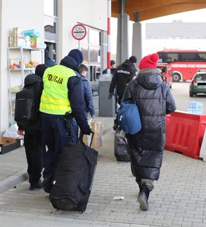 Policjant pomagający kobiecie nieść walizkę.