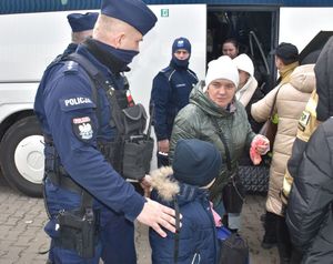 Policjant przed autobusem pomaga wysiąść pasażerom