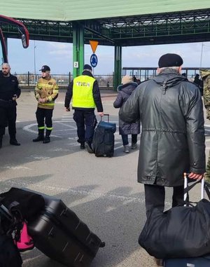 Zdjęcie kolorowe przedstawia policjanta który pomaga uchodźcom z Ukrainy  w przenoszeniu bagaży