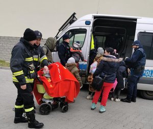 Policjanci i strażacy pomagający wsiąść dzieciom do radiowozu.