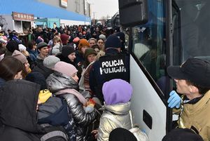 Policjant przy autobusie. Przed nim tłum ludzi.