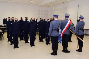 Na pierwszym planie poczet sztandarowy (widok od tyłu), w tle ślubujący policjanci.