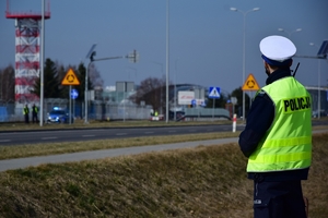 Policjant ruchu drogowego (po prawej stronie). W tle budynki i infrastruktura lotniska.