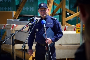 Policjant przy mikrofonie. W tle plac budowy.