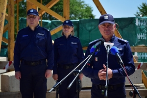 Komendant Wojewódzki Policji w Rzeszowie stoi przy mikrofonie, w tle policjant i policjantka, plac budowy.