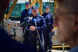 Komendant Wojewódzki Policji w Rzeszowie stoi przy mikrofonie, w tle policjant i policjantka, plac budowy.