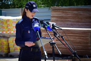 Policjantka przy mikrofonie, w tle plac budowy.