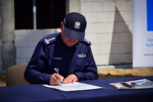 Policjant przy stole podpisuje akt erekcyjny. W tle plac budowy