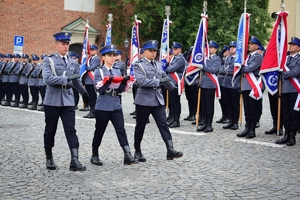 Poczet sztandarowy maszeruje widok od przodu w tle policyjny sztandary i kompania honorowa.