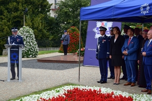 Po lewej Komendant Wojewódzki Policji w Rzeszowie przy mównicy przy mikrofonie. Po prawej Komendant Główny Policji oraz zaproszeni goście pod namiotem.