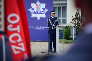 Komendant Główny Policji w centrum kadru przy mikrofonie, w tle banner z policyjną gwiazdą.