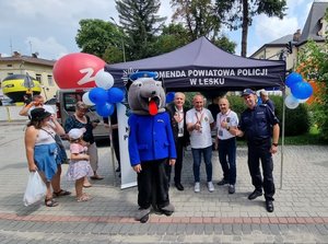 Namiot z napisem Komenda Powiatowa Policji w Lesku, obok namiotu po prawej stoi policjant oraz kilka osób. Na pierwszym planie policyjna maskotka - wilczek.