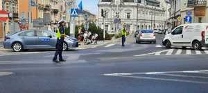 Na pierwszym planie policjantka kierująca ruchem. Po prawej policjant stojący na skrzyżowaniu i jadące samochody.