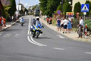 Policyjne motocykle dojeżdżające do zakrętu drogi. Na chodnikach wzdłuż drogi kibice.