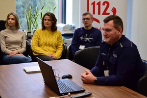 Policjanci i pracownicy CPR podczas szkolenia. Uczestnicy siedzą przy stole, przed nimi ekran z kamerą.