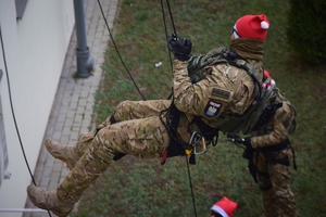 Policyjni antyterroryści z prezentami, w czapkach mikołajkowych zjeżdżają na linach z dachu budynku do szpitalnego okna