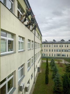 Policyjni antyterroryści z prezentami, w czapkach mikołajkowych zjeżdżają na linach z dachu budynku do szpitalnego okna