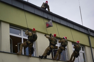 Policyjni antyterroryści z prezentami, w czapkach mikołajkowych zjeżdżają na linach z dachu budynku do szpitalnego okna