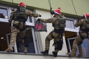 Policyjni antyterroryści z prezentami, w czapkach mikołajkowych zjeżdżają na linach z dachu budynku do szpitalnego okna