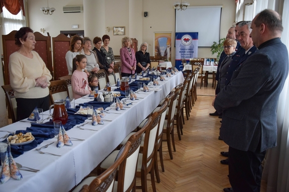 Policjanci podczas spotkania z rodzinami poległych policjantów. Uczestnicy spotkania dzielą się opłatkiem i składają sobie życzenia przy wigilijnym stole.