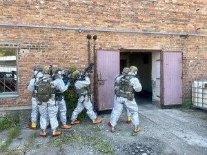 umundurowani policyjni kontrterroryści  w szyku bojowym, z bronią wchodzą do budynku