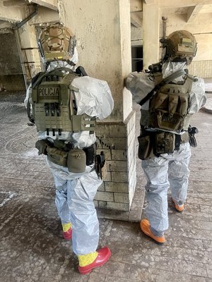 mundurowani policyjni kontrterroryści  w szyku bojowym, z bronią sprawdzają pomieszczenia wewnątrz budynku
