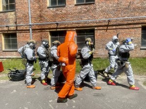 osoba w specjalistycznym kombinezonie w kolorze pomarańczowym, w tle pododdział umundurowanych policyjnych kontrterrorystów
