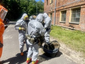 osoba w specjalistycznym kombinezonie w kolorze pomarańczowym, w tle pododdział umundurowanych policyjnych kontrterrorystów