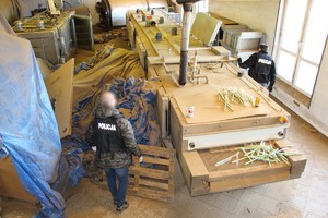 Dwaj policjanci ubrani w czarne kamizelki z białym napisem &quot;policja&quot; stoją po dwóch stronach dużej maszyny używanej do produkcji papierosów