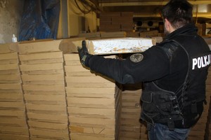 Policjant ubrany w czarną kamizelkę z białym napisem &amp;quot;policja&amp;quot; trzyma karton z papierosami, w tel inne kartony