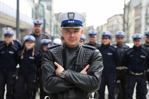 policjant ruchu drogowego w białej czapce i skórzanym mundurze policyjnym na motocykl stoi na tle grupy policjantów