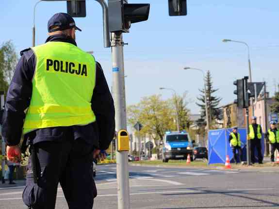 policjant stoi przy sygnalizatorze w oddali rozstawiony parawan i stoia policjanci