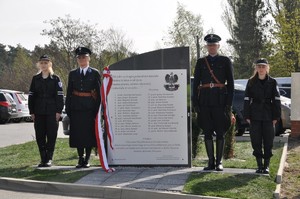 Po bokach obelisku stoją policjant i policjantka w mundurach Policji Państwowej, obok nich stoją uczeń i uczennica klasy mundurowej.