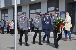 Delegacja z Komendantem Wojewódzkim, przed nimi policjant niosący wieniec, który mają złożyć przed obeliskiem.