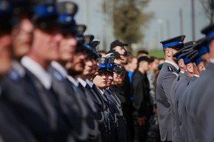 Dwuszereg policjantów, ostrość  skupiona na twarzy policjantki stojącej w głębi.