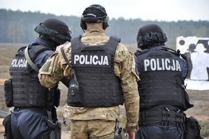 Trzech policjantów stoi tyłem, widać biały napis policja