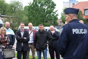 Na pierwszym planie policjant tyłem, a w tle pani i usmiechnięci mężczyźni.