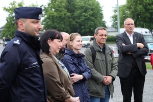 Na pierwszym planie umundurowany policjant, a za nim stoją panie i panowie - zdjęcie zrobione bokiem