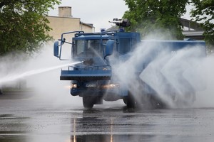 Policyjna polewaczka jadąca do przodu i tryskająca wodą.