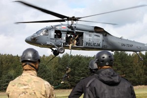 Policyjni zamaskowani kontrterroryści i Black Hawk w tle z którego na linie desantuje się policjant