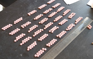 Na stole leży kilkadziesiąt ułożonych w rzędach tabletek koloru różowego