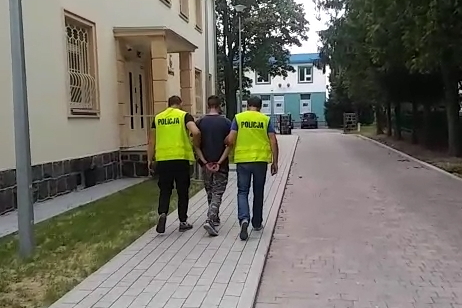 Zdjęcie przedstawia dwóch policjantów, którzy prowadzą zatrzymanego.