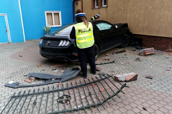 Miejsce zdarzenia drogowego w Szczytnie. Rozbity samochód przy budynku, obok policjanci