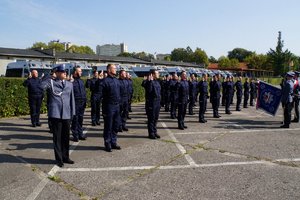 Uczestnicy uroczystego ślubowania nowo przyjętych policjantów. Policjanci stojący w szeregu wypowiadają słowa Roty. Przed nimi stoi Poczet Sztandarowy.