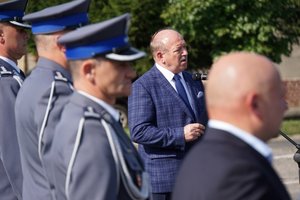 Uczestnicy uroczystego ślubowania nowo przyjętych policjantów. Na pierwszym planie zastępca Wojewody Aleksander Socha stojący przed mikrofonem. Na drugim planie stojący oficerowie policji.